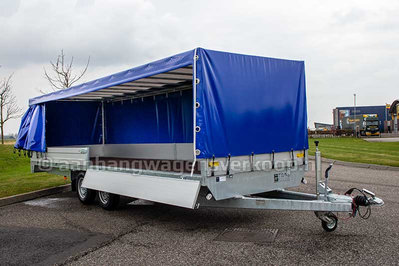 Tandemas plateauwagen met geopende blauwe huif en neergeklapt bord